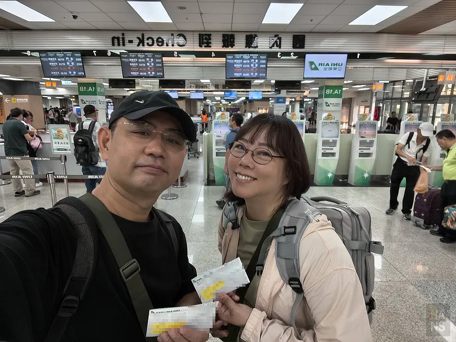 翰斯與 Kay 在台北松山機場立榮航空櫃檯前，拿著登機證自拍