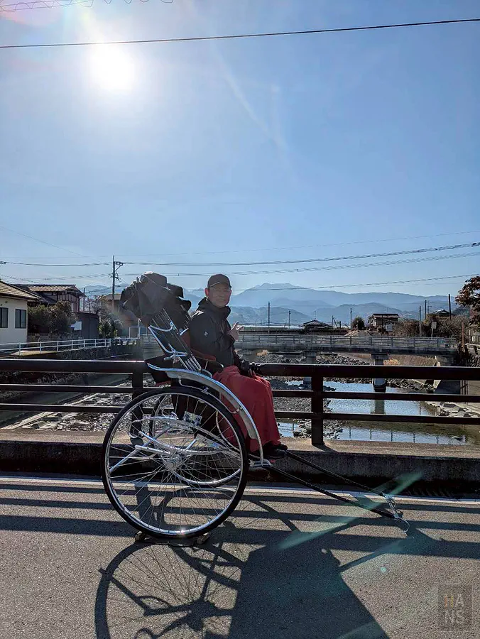 翰斯坐在人力車上於太良町橋上與山景藍天合照