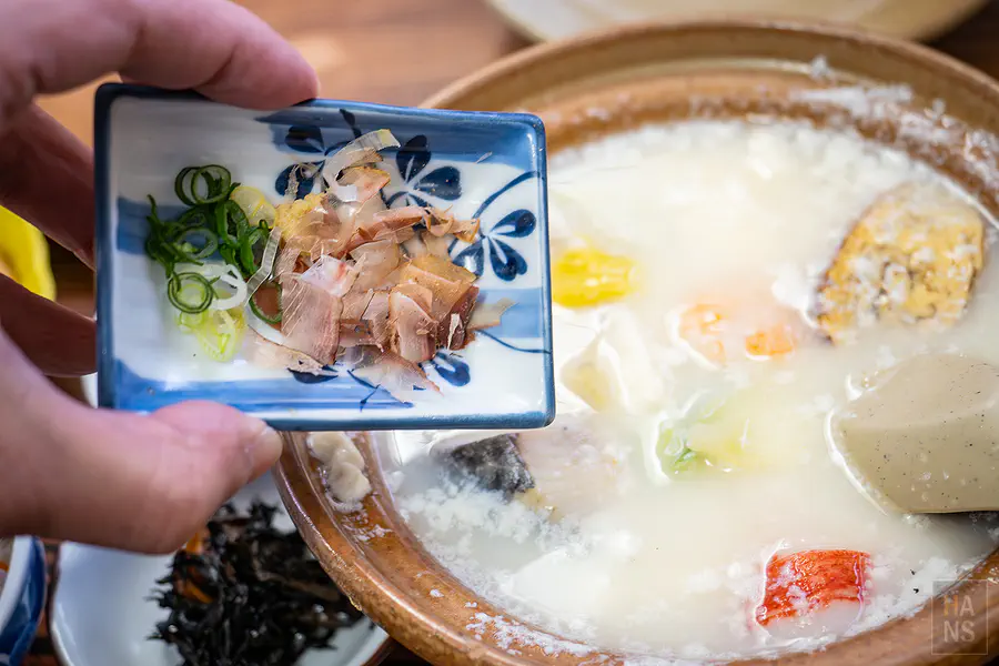 將柴魚片與蔥花佐料加入溫泉湯豆腐鍋中提味