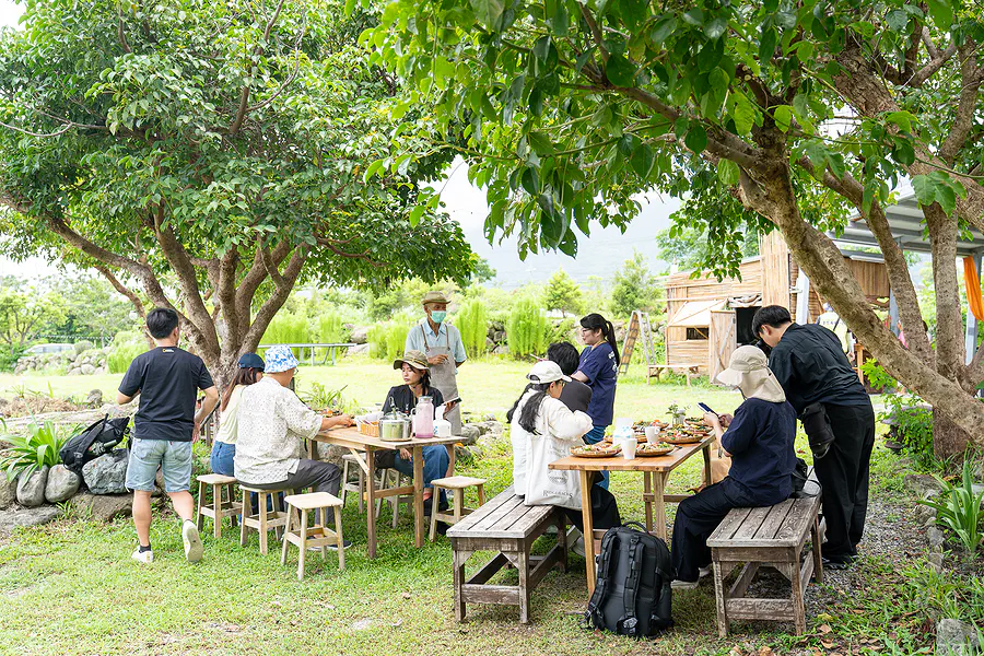 藝蔬咖食坊戶外大樹下的用餐區，旅人們圍著木桌用餐