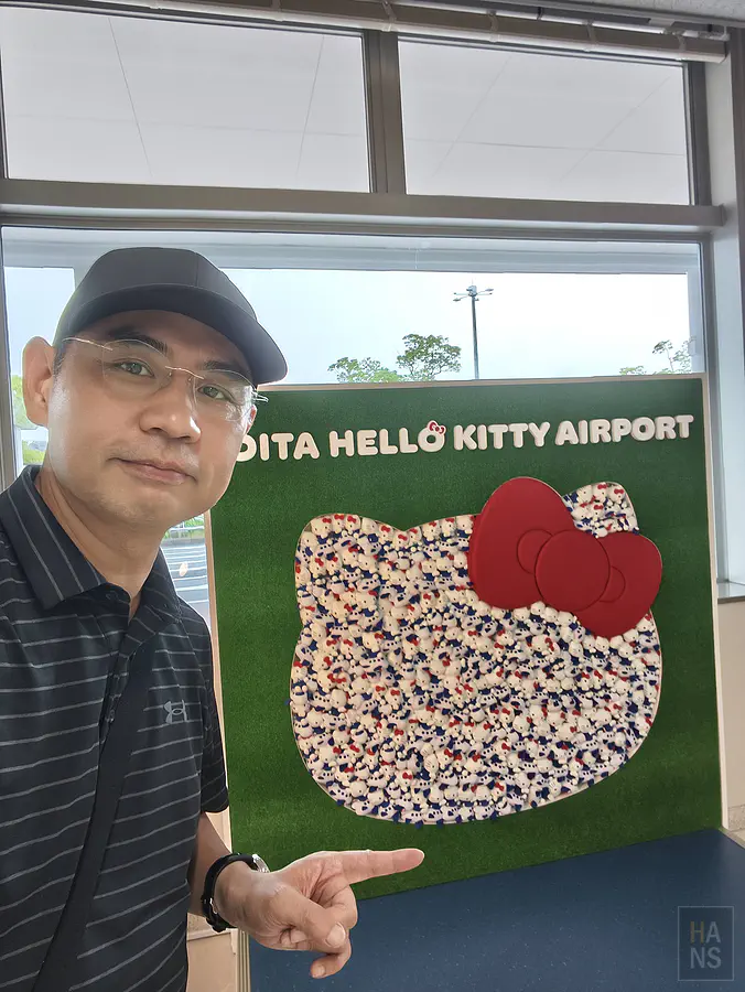 翰斯與大分 Hello Kitty 機場玩偶牆自拍合影