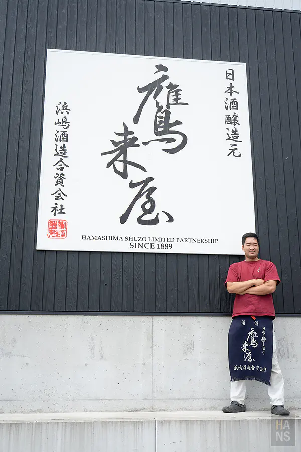 鷹來屋六代目繫藍染前掛於看板前留影