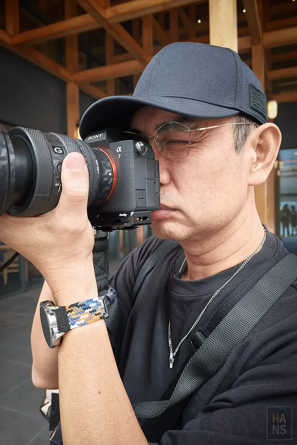 翰斯拿著 Sony 相機拍照時胸前掛著 AWNL 隕石項鍊的側面