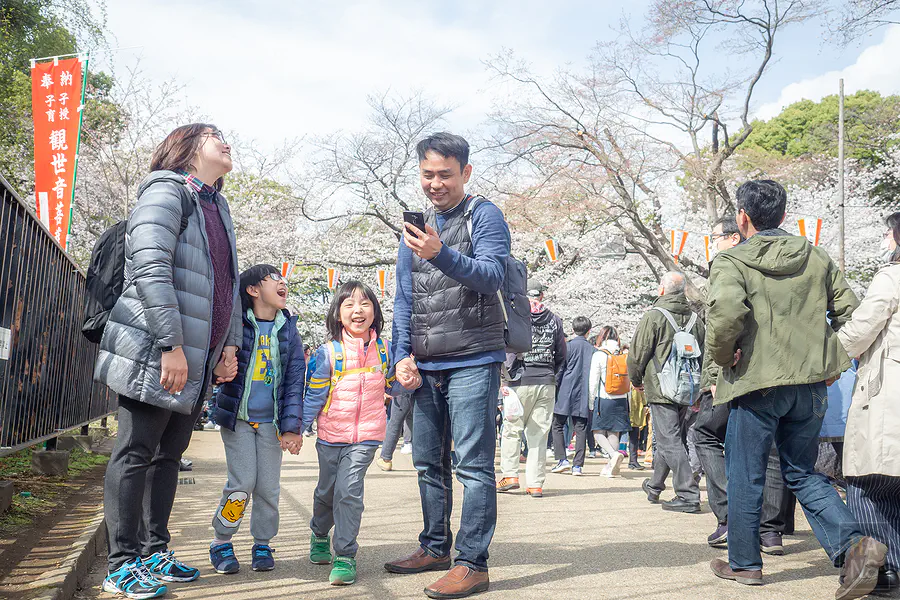 翰斯一家在上野公園櫻花樹下散步，兩個女兒開心笑鬧的自然瞬間