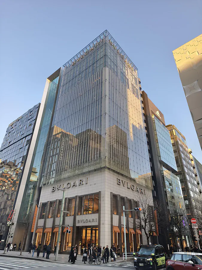 銀座中央通 BVLGARI 旗艦店大樓，傍晚陽光下的玻璃帷幕與街道行人